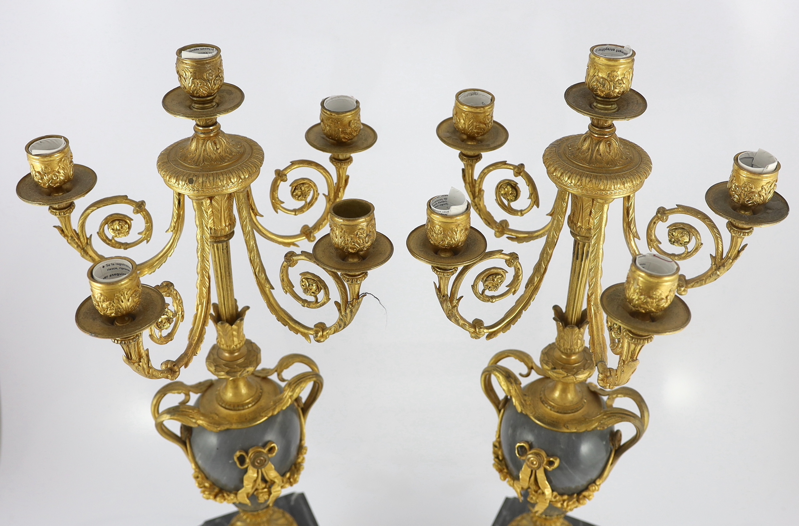 A pair of Louis XVI style ormolu and grey marble five light candelabra, with scrolling branches and urn shaped stems on architectural plinths, 26cm wide, 63cm high